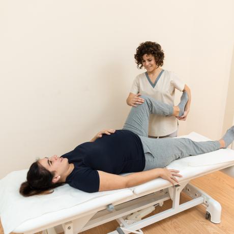 Side view of a pregnant woman lying on a massage table while a physiotherapist massages her legs at a health center. Concept of massage for pregnant.