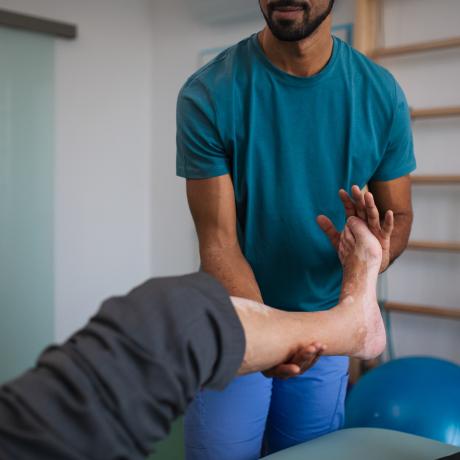 A close-up of physiotherapist exercising with senior patient's leg in a physic room.